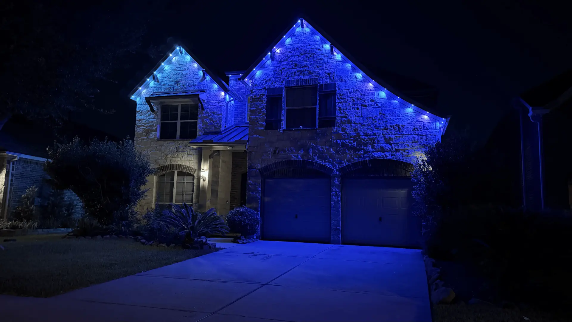 Blue permanent LED roofline lighting on a Houston stone home at night